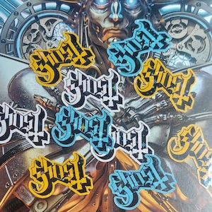 May include: A collection of nine holographic stickers featuring the word "Ghost" in a stylized font. The stickers are in various shades of blue, yellow, and white with a glittery finish.