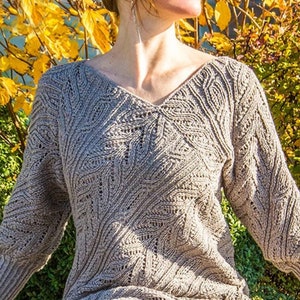 May include: A light brown knitted dress with a V-neck and long sleeves. The dress features a detailed, open-knit pattern. The sleeves have a ribbed cuff and a slightly puffed design. The dress is knee-length and appears to be made of a soft, textured yarn.