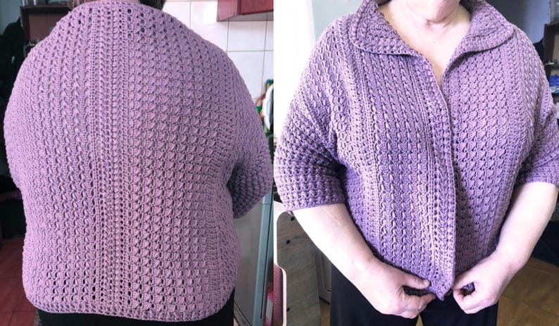 May include: A lavender-colored, crocheted cardigan with a collar and short sleeves. The front of the cardigan has a button closure. The crochet pattern is visible throughout the garment.
