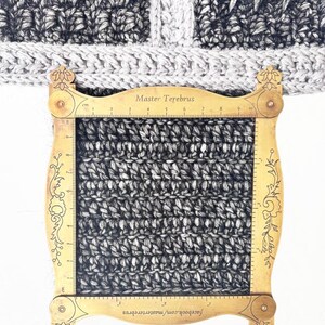 May include: A close-up of a knitted fabric sample in shades of gray and white, with a wooden gauge tool placed over it. The gauge tool has measurements in centimeters and the text "Master Terebrus" and "GAUGE for cardigan and sweater".