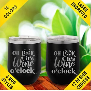 May include: Two black stemless wine tumblers with silver rims and lids. The tumblers have the phrase "OH LOOK it's Wine o'clock" etched on them. The image also includes text that says "16 COLORS", "LASER ENGRAVED", "3 MUG STYLES", and "12 DESIGN CHOICES".