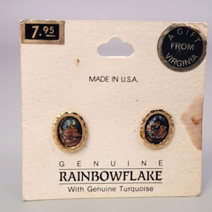 May include: A pair of oval stud earrings with gold-toned scalloped edges and dark centers containing flecks of turquoise. The earrings are mounted on a white display card labeled "GENUINE RAINBOWFLAKE With Genuine Turquoise" and "MADE IN U.S.A."