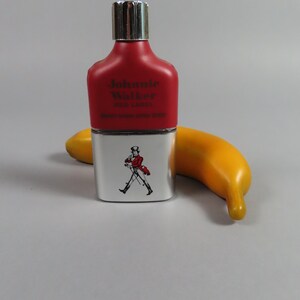 May include: A red and silver flask with the text "Johnnie Walker RED LABEL" and a graphic of a man walking. A yellow banana is next to the flask.