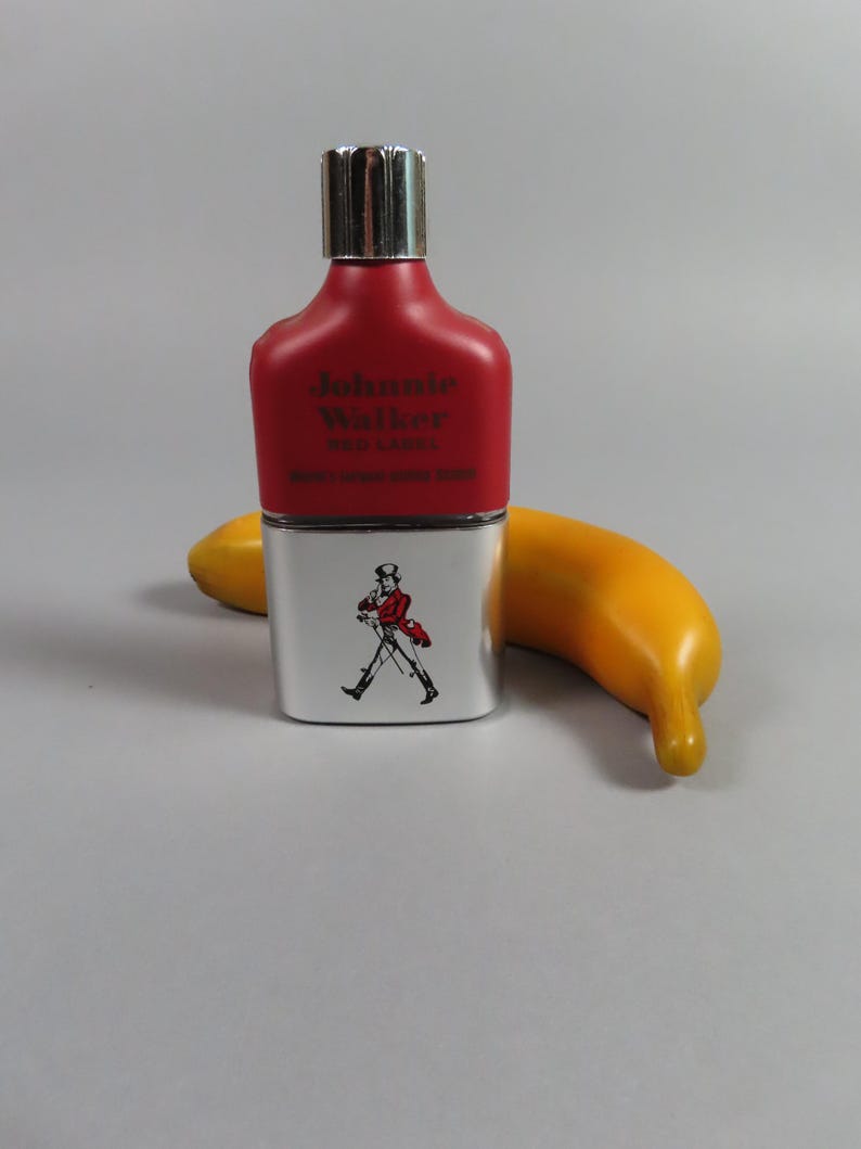 May include: A red and silver flask with the text "Johnnie Walker RED LABEL" and a graphic of a man walking. A yellow banana is next to the flask.