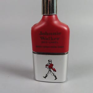 May include: A red and silver Johnnie Walker Red Label bottle. The top portion is red with the brand name and label text. The bottom is silver with a graphic of a man in a red coat walking. The bottle has a silver cap.