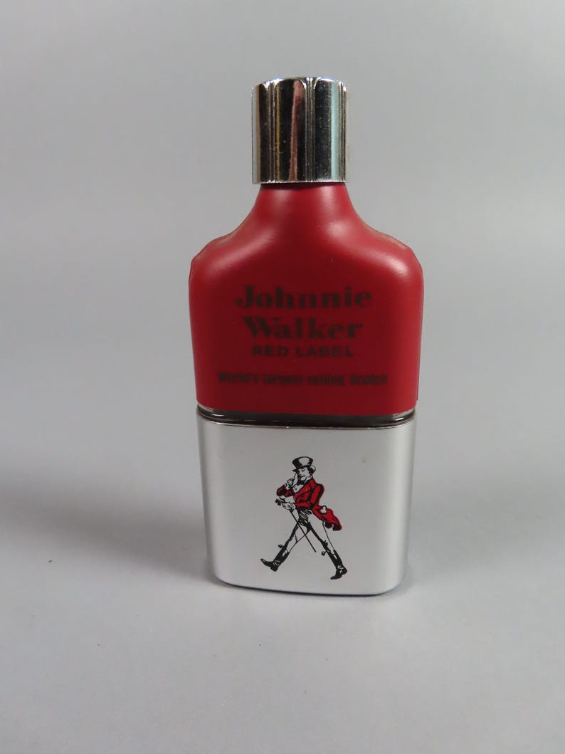 May include: A red and silver Johnnie Walker Red Label bottle. The top portion is red with the brand name and label text. The bottom is silver with a graphic of a man in a red coat walking. The bottle has a silver cap.