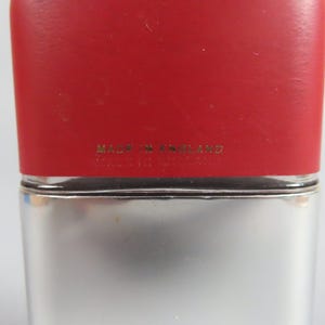 May include: A rectangular flask with a red top and a silver-colored body. The text "MADE IN ENGLAND" is printed in gold lettering on the red top. The flask has a simple, classic design.