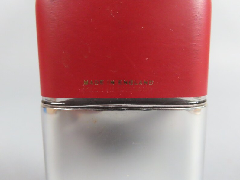 May include: A rectangular flask with a red top and a silver-colored body. The text "MADE IN ENGLAND" is printed in gold lettering on the red top. The flask has a simple, classic design.