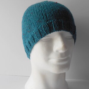 May include: A teal blue knitted beanie with red flecks. The beanie is made of a soft, warm material and has a simple, classic design.