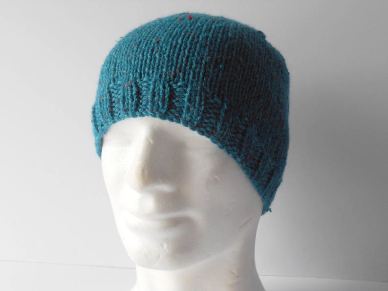 May include: A teal blue knitted beanie with red flecks throughout the fabric. The beanie is on a white mannequin head.