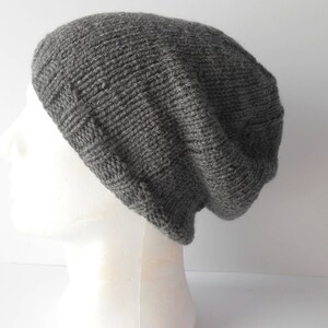 May include: A gray knitted beanie hat with a slouchy fit. The hat is made of a soft, textured yarn.