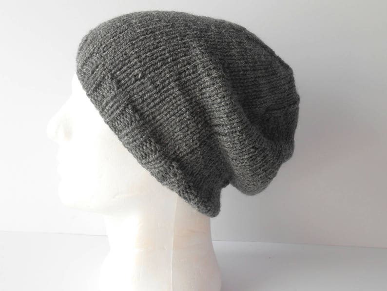 May include: A gray knitted beanie hat with a slouchy fit. The hat is made of a soft, textured yarn.