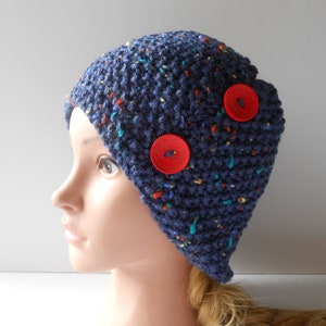 Puede incluir: Un gorro azul de punto con botones rojos. El gorro tiene un patrón moteado con motas multicolores.