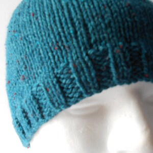 May include: A teal blue knitted beanie with red flecks throughout the fabric.
