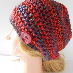 Puede incluir: Un gorro de punto de color rojo, azul y naranja con un botón grande de color rojo en el lateral.