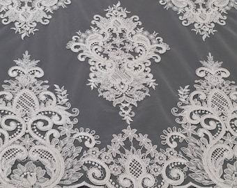 May include: White lace fabric with a delicate floral pattern. The lace is embroidered on a sheer mesh background. The fabric has a scalloped edge.