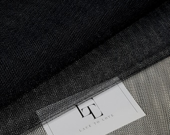 Peut inclure: Un morceau de tissu tulle noir avec une texture en maille fine. Une étiquette rectangulaire blanche est fixée au tissu, présentant un logo noir avec les lettres LT et le texte LACE TO LOVE imprimé dans une police sans empattement.