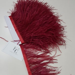 Puede incluir: Borde de plumas de avestruz rojo con un respaldo de cinta de satén rojo. El borde tiene aproximadamente 2,5 cm de ancho. El borde está etiquetado como "Lace to Love."