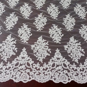 May include: A white lace fabric featuring a repeating floral pattern of embroidered blossoms and leaves. The material has a sheer mesh base and a scalloped decorative border along the bottom edge, showcasing intricate needlework throughout.