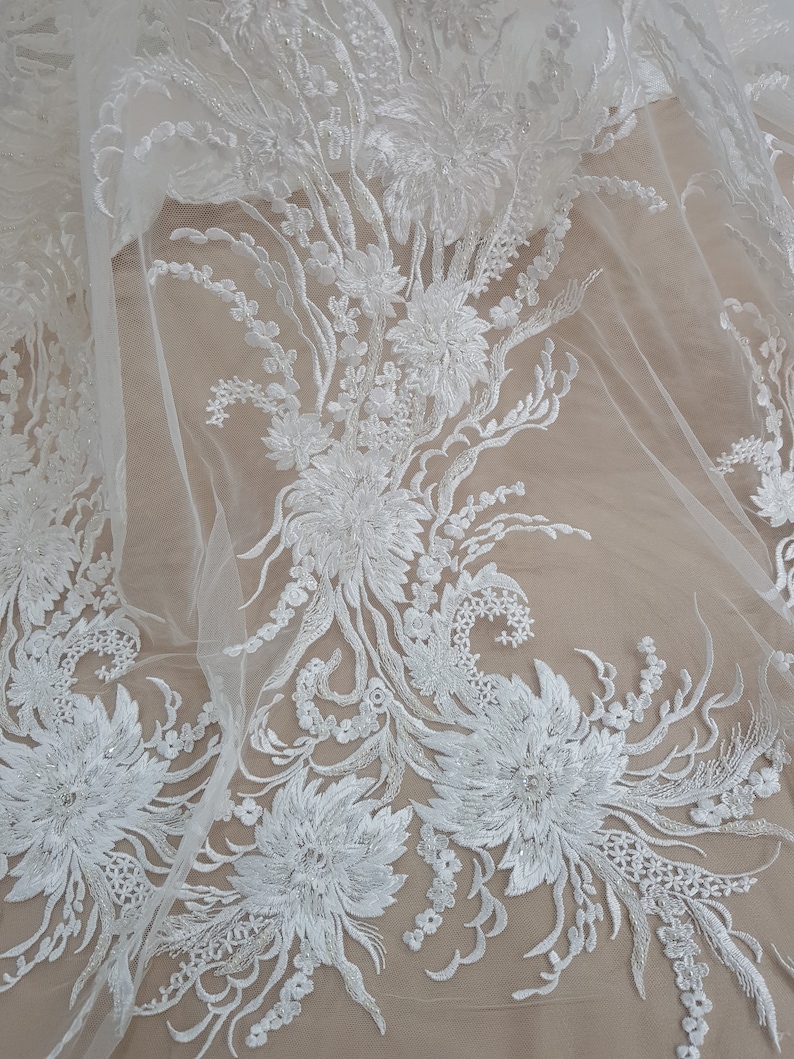 Puede incluir: Tela de encaje floral blanca con un delicado patr&oacute;n de flores y hojas. El encaje est&aacute; sobre un fondo de malla transparente.