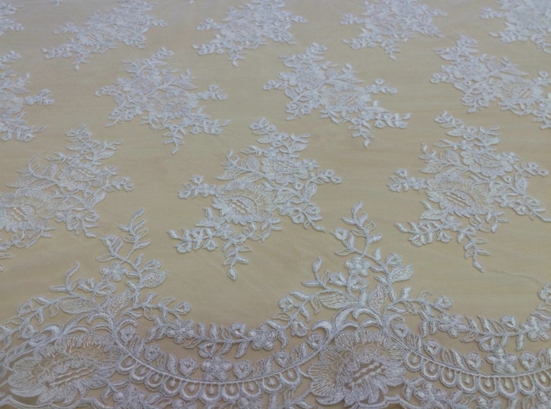 May include: White floral lace fabric with a delicate pattern. The lace is on a beige background.
