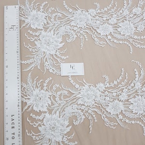 Puede incluir: Tela de encaje floral blanca con un delicado patr&oacute;n de flores y hojas. El encaje est&aacute; sobre un fondo de malla transparente.