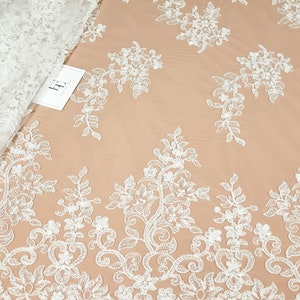 May include: White floral lace fabric with a delicate pattern of flowers and leaves. The lace has a scalloped edge and is perfect for adding a touch of elegance to any project.