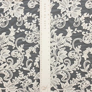 May include: Off-white lace fabric featuring an intricate floral and vine pattern with embroidered details. A white ruler labeled LACE TO LOVE is placed vertically over the fabric, showing measurements in both inches and centimeters.