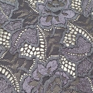 Puede incluir: Primer plano de una tela de encaje gris oscuro con un patr&oacute;n floral. El encaje tiene un dise&ntilde;o delicado e intrincado con peque&ntilde;as flores en relieve.