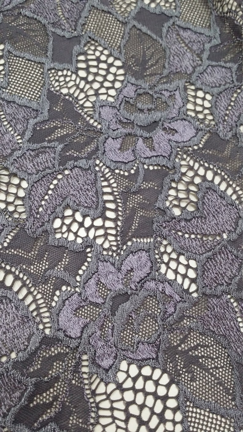 Puede incluir: Primer plano de una tela de encaje gris oscuro con un patr&oacute;n floral. El encaje tiene un dise&ntilde;o delicado e intrincado con peque&ntilde;as flores en relieve.
