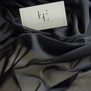 May include: A white card with the text "Lace to Love" and a monogrammed "LT" logo in a black square. The card is lying on a black sheer fabric.