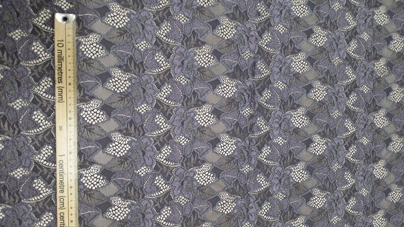 Puede incluir: Tela de encaje gris con un patr&oacute;n floral. La tela tiene un detalle de cuentas blancas y una regla para la escala.