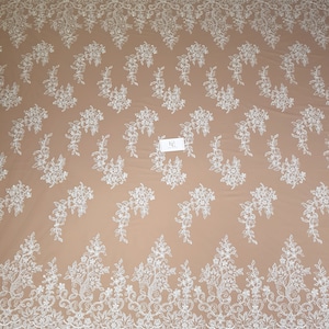 May include: White floral lace fabric with a delicate pattern. The lace has a scalloped edge and is perfect for crafting, sewing, or decorating.