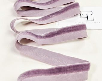 Puede incluir: Primer plano de una bobina de cinta de terciopelo lavanda con borde de satén. La cinta está doblada y dispuesta sobre una superficie blanca. El texto "Lace to Love" es visible en una tarjeta blanca en el fondo.