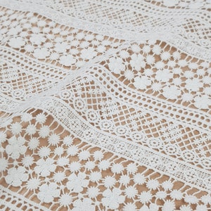 May include: White crochet fabric with a delicate floral pattern. The fabric has a textured, lacy appearance and is perfect for crafting or sewing projects.