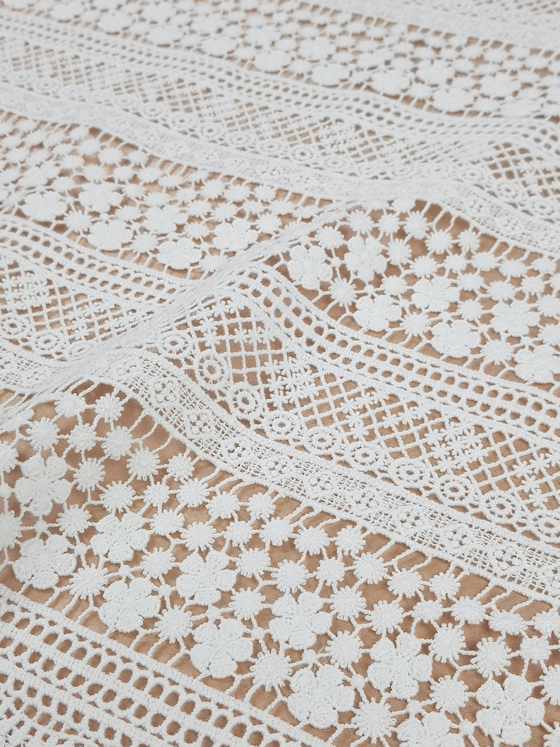 May include: White crochet fabric with a delicate floral pattern. The fabric has a textured, lacy appearance and is perfect for crafting or sewing projects.