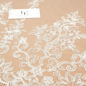 May include: White floral lace fabric with a delicate pattern. The lace is on a beige background. The text "Lace to Love" is visible on a white card.