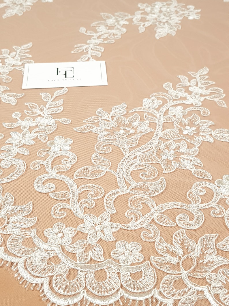 May include: White floral lace fabric with a delicate pattern. The lace is on a beige background. The text "Lace to Love" is visible on a white card.