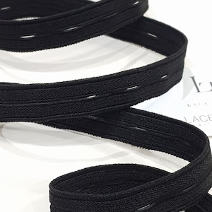 May include: Close-up of black elastic band with stitched detailing. The band is flexible and has a ribbed texture, with parallel lines of stitching. The elastic is curved and appears to be new.