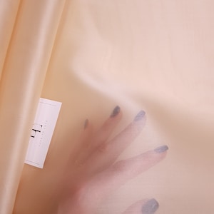 Könnte beinhalten: Ein durchsichtiger, pfirsichfarbener Stoff mit einer glatten, seidenartigen Textur. Der Stoff ist über eine weiße Oberfläche drapiert, auf der sich eine kleine weiße Karte mit der Aufschrift "Lacy to Love" befindet.