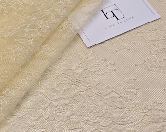 May include: A cream-colored lace fabric featuring a delicate floral pattern with intricate embroidery and a fine mesh base. A white rectangular card is placed on the fabric with the black text LACE TO LOVE and a stylized logo printed on it.