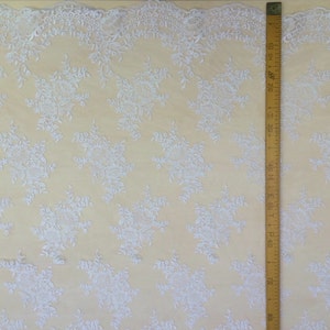 May include: White lace fabric with a delicate floral pattern. The fabric is shown next to a ruler measuring 30 inches.