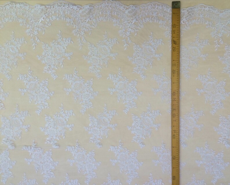 May include: White lace fabric with a delicate floral pattern. The fabric is shown next to a ruler measuring 30 inches.