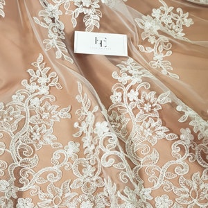 May include: White floral lace fabric with a delicate pattern. The lace is on a sheer mesh background. The fabric is perfect for wedding dresses, bridal accessories, and other special occasion garments.