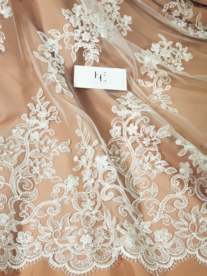 May include: White floral lace fabric with a delicate pattern. The lace is on a sheer mesh background. The fabric is perfect for wedding dresses, bridal accessories, and other special occasion garments.