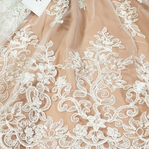 May include: White floral lace fabric with a delicate pattern. The lace is on a sheer mesh background.