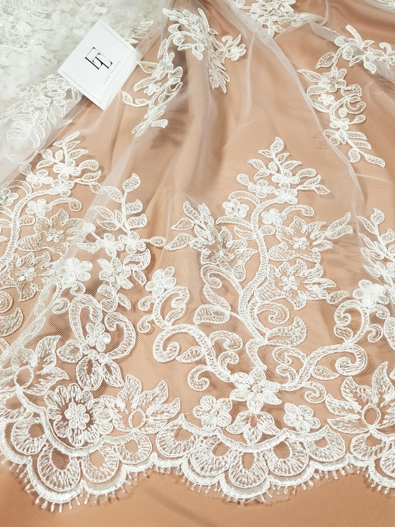 May include: White floral lace fabric with a delicate pattern. The lace is on a sheer mesh background.