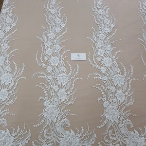 Puede incluir: Tela de encaje floral blanca con un dise&ntilde;o delicado e intrincado. El encaje presenta un patr&oacute;n repetitivo de flores y hojas, creando un aspecto fluido y elegante.