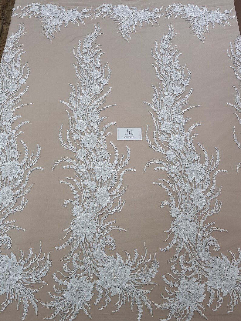 Puede incluir: Tela de encaje floral blanca con un dise&ntilde;o delicado e intrincado. El encaje presenta un patr&oacute;n repetitivo de flores y hojas, creando un aspecto fluido y elegante.