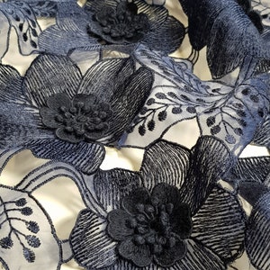 May include: A navy blue floral lace fabric featuring intricate three-dimensional embroidered flower petals and delicate vine patterns. The design consists of layered dark blue thread work on a sheer, lightweight mesh base, creating a textured surface.